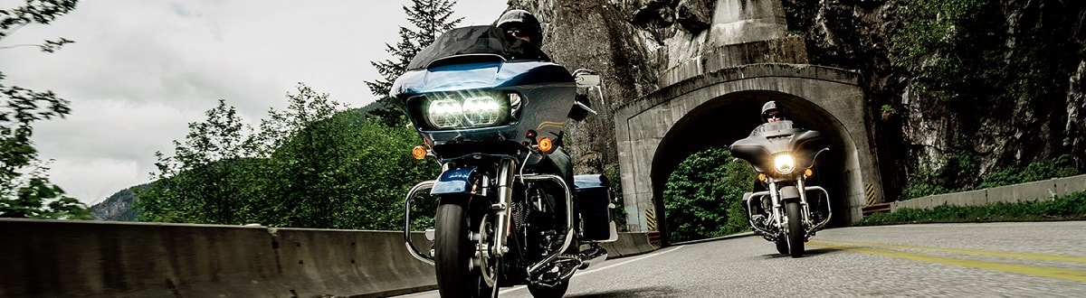 Two Individuals riding on Harley-Davidson CVO motorcycles through a mountain highway tunnel on a grey day.